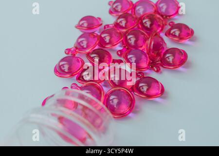 Aus einer Plastikflasche verschüttete Serumkapseln für trockenes, geschädigtes und krauses Haar. Nahaufnahme hellblauer Hintergrund Stockfoto