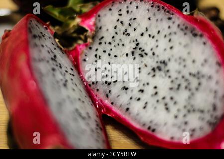 Frisch geschnittene Drachenfrucht (pitaya) mit leuchtend rosa Haut und gesprenkeltem weißem Fruchtfleisch auf einer Holzoberfläche Stockfoto