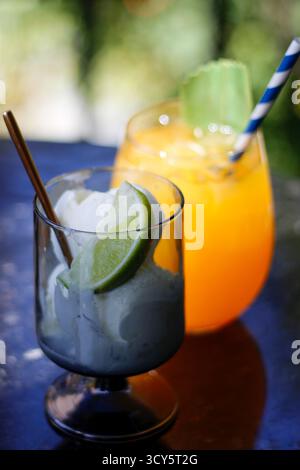 Zwei erfrischende Sommergetränke auf einem Tisch, einer mit Orangensaft und der andere mit Limette und Schlagsahne. Hochwertige Fotos Stockfoto