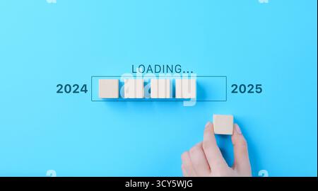 Ladefortschrittsleiste von 2024 bis 2025 mit Holzblöcken. Eine Hand platziert Holzblöcke in einer Reihe, wodurch ein Übergang mit einem Fortschrittsbalken erstellt wird Stockfoto
