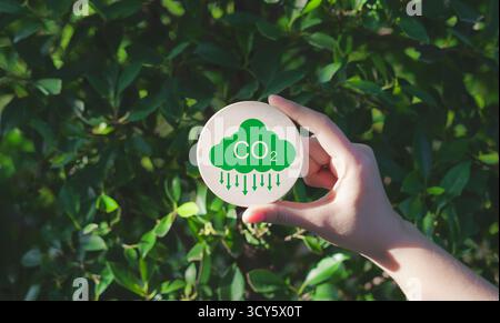 Konzept zur Reduzierung der CO2-Emissionen. Eine Hand hält ein grünes CO2-Emissionssymbol, das das Bewusstsein für den CO2-Fußabdruck, den Netto-Nullwert und die CO2-Neutralität repräsentiert. Stockfoto