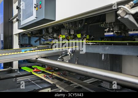Skischuhe, die an Skier gebunden sind, auf einer automatisierten industriellen Produktionslinie in einer Fabrik. Stockfoto