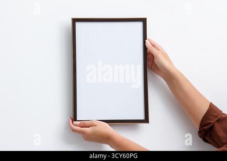 Frau, die einen leeren Diplomrahmen an der weißen Wand hängt, Großaufnahme. Modell für Design Stockfoto