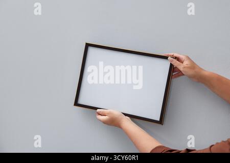 Frau, die einen leeren Diplom-Rahmen an einer Lichtwand hängt, Großaufnahme. Modell für Design Stockfoto