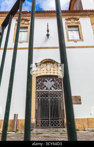 Ein Blick durch dunkelgrüne Eisenstangen offenbart ein großes weißes Gebäude mit einem verzierten Eingang und dekorativen Fenstern unter blauem Himmel Stockfoto