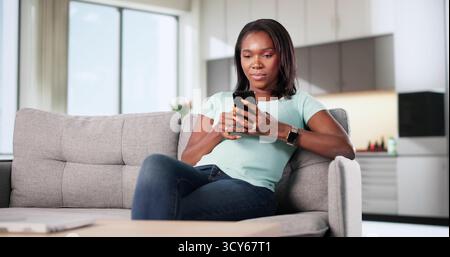 Lächelnde Frau Sitzt Auf Der Couch, Hält Ihr Smartphone Und Chatte Online. Stockfoto