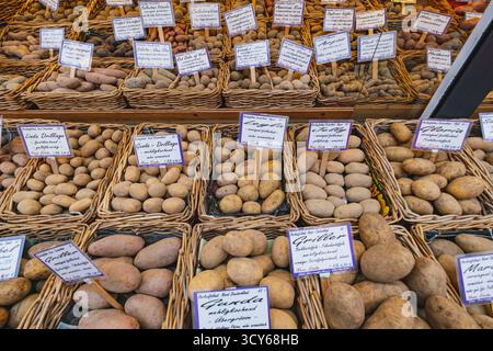 Ein Marktstand, an dem verschiedene Kartoffelsorten in Korbkörben mit handgeschriebenen Etiketten und Preisen präsentiert werden Stockfoto