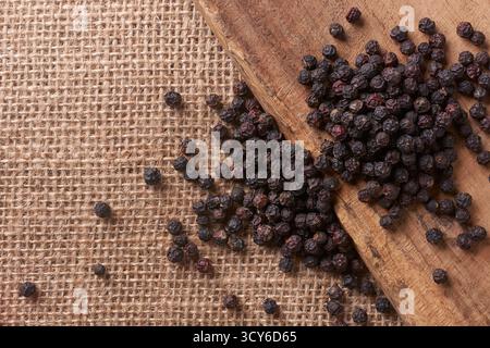 Schwarze Pfefferkörner auf Holzplanken und Sackleinen, rustikale Texturen mit Kopierraum für Text, Konzepte von kulinarischem Gewürz Stockfoto