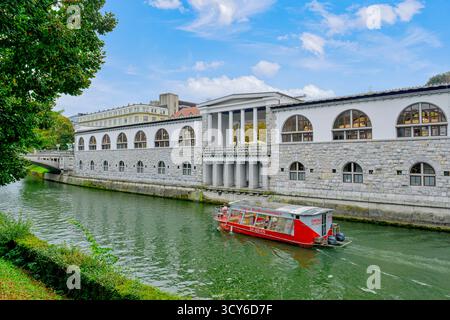 Blick auf die Touristenboote auf der Ljubljanica, Cafés und andere Gebäude entlang der Uferpromenade in Ljubljana, Slowenien Stockfoto