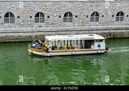 Blick auf die Touristenboote auf der Ljubljanica, Cafés und andere Gebäude entlang der Uferpromenade in Ljubljana, Slowenien Stockfoto