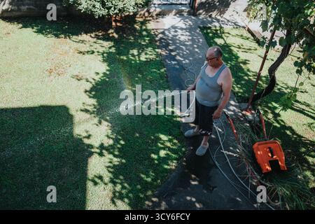 Man bewässert Rasen mit Schlauch im sonnigen Garten im Garten im Sommer Stockfoto