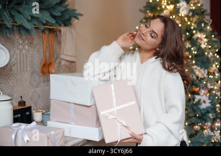Frau in kuscheliger Pullover, die Geschenke in der Nähe des Weihnachtsbaums hält. Stockfoto