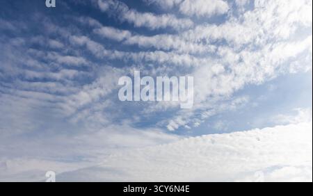Heller Himmel mit verstreuten weißen Wolken vor tiefblauem Hintergrund. Eine ruhige, offene Atmosphäre, perfekt für Natur, Reisen und Outdoor-Aktivitäten Stockfoto