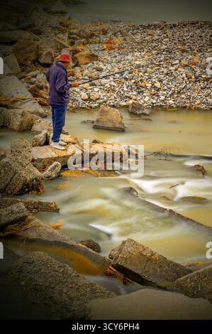 Bacau, Rumänien, 13. Juni 2016: Eine Person steht auf einem großen Felsen in der Nähe eines fließenden Flusses und beobachtet das Wasser. Lange Belichtung erzeugt einen seidigen Effekt. Stockfoto