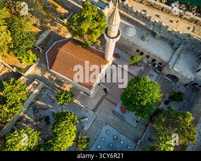 Blick aus der Vogelperspektive auf eine historische Zitadelle am Meer mit einem Steinminarett und zinnenbesetzten Wänden im goldenen Sonnenlicht. Stockfoto