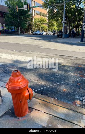 Auf dem Gehweg vor einem Gebäude befindet sich ein roter Hydrant. Der Hydrant ist orange und befindet sich am Straßenrand Stockfoto