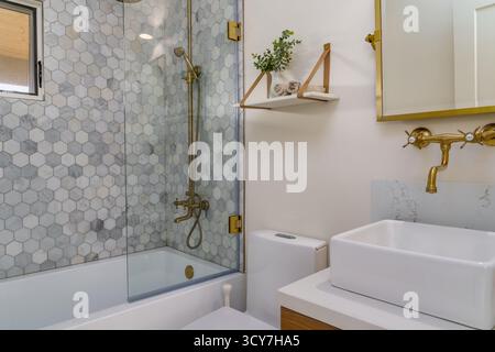Modernes Bad mit Dusche, sechseckiger Fliese, Glaswand und goldenen Messingarmaturen Stockfoto