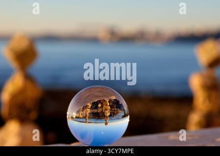 Kristallkugel auf einem Küstenvorsprung mit umgekehrter Sicht auf Steinhaufen und blaues Wasser in Lissabon, Portugal, gefangen zur goldenen Stunde mit flachem DOF. Stockfoto