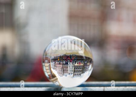 Glass ball on a canal bridge showing an inverted red bicycle and townhouses, photographed with shallow depth of field and a blurred urban backdrop. Stockfoto