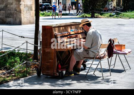 Barcelona, ​​Spain, 3. August 2025: Ein Straßenmusiker tritt an einem hellen sonnigen Tag auf einem alten mobilen Klavier auf. Ein Einblick in das Leben in der Großstadt. Stockfoto