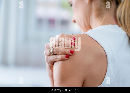 Schulterschmerzen werden durch eine Frau angezeigt, die ihre Schulter hält. Stockfoto