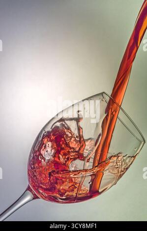 Geneigtes Weinglas wird mit roter Flüssigkeit gefüllt. Spritzer und Wellen heben Bewegung, Transparenz und Strömungsdynamik in einer raffinierten Komposition hervor. Stockfoto