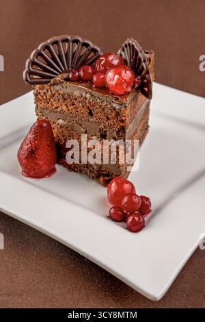 Schokoladenkuchen in Lagen mit roten Johannisbeeren, glasierten Erdbeeren und Einrichtung in Ventilatorform. Satte Töne und elegante Beschichtung. Stockfoto