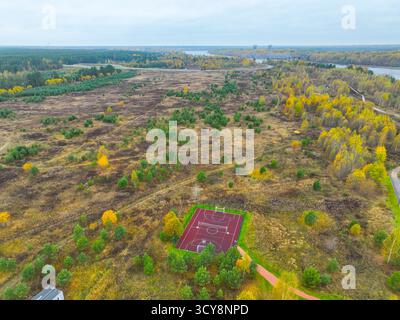 Weite Luftaufnahme eines roten Basketballplatzes im Freien auf einem großen, offenen Feld, umgeben von Büschen und Herbstwald Stockfoto
