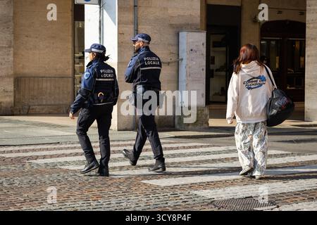 Zwei italienische Polizeibeamte in dunklen Uniformen laufen während ihrer Patrouille über einen Fußgängerübergang auf einer Kopfsteinpflasterstraße Stockfoto