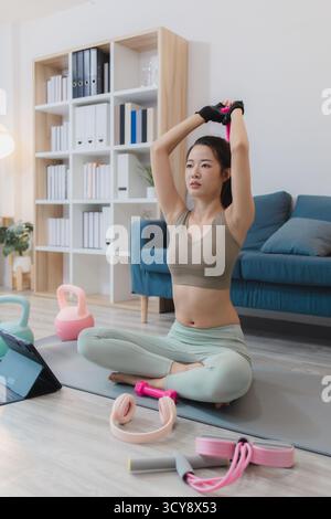 Eine junge Frau trainiert zu Hause, übt Yoga und Krafttraining mit Kurzhanteln und Kettlebells auf einer Matte. Sie folgt ihrer Trainingsroutine wi Stockfoto
