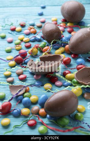Foto-Hälften Schokolade Eiern, bunte Pralinen, auf blauen Holztisch Stockfoto