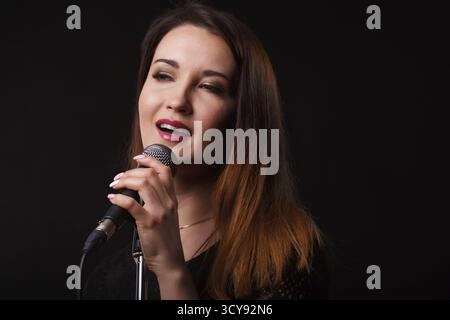 Junge Frau mit Mikrofon auf dem Hintergrund von Rauch im Studio Stockfoto