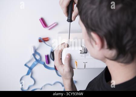 Mann mit Schraubenzieher Reparatur Nähmaschine auf leeren grauen Hintergrund Stockfoto