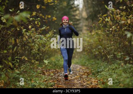 Porträt in vollem Wachstum, die jungen Athleten im Trainingsanzug im bunten Wald laufen lassen. Glückliche Model-Frau in Bewegung Stockfoto