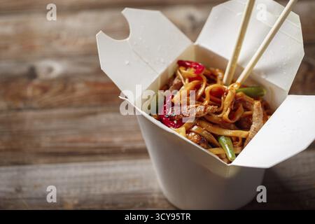 Nudeln mit Schweinefleisch und Gemüse in der Take-out-Box auf Holztisch. Draufsicht Stockfoto