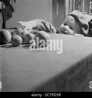 Ein liebenswertes Archivfoto aus den 1960er Jahren zeigt ein neugieriges Kleinkind in Sloviansk, der ukrainischen SSR. Mit einer charmanten Baskenmütze liegt das Baby auf seinem Bauch und greift gespannt nach Äpfeln, die auf einem Tisch verstreut sind. Die Szene, die wahrscheinlich in einem gemütlichen Zuhause spielt, erinnert an die einfachen Freuden und Entdeckungen der frühen Kindheit. Dieser intime Schnappschuss ist ein herzerwärmender Einblick in den Familienalltag während der Sowjetzeit, eine nostalgische Aufzeichnung friedlicher Momente im Donbass vor dem Krieg Stockfoto