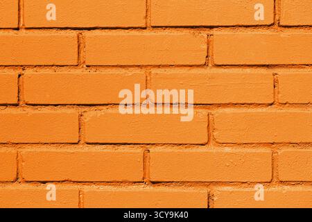 Nahaufnahme der orangen Ziegelwand. Heller gemalter Backsteinhintergrund mit geometrischem Muster und rauer Oberfläche. Stockfoto