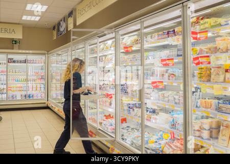 Lombardei, Italien - 2. Juli 2025 Frau wählt Milchprodukte aus einer gekühlten Vitrine in einem hellen, modernen Lebensmittelgeschäft, das Lebensmittel kauft Stockfoto