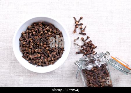 Getrocknete Nelken, in einer weißen Schüssel, auf Leinen. Aromatische Blütenknospen des Baumes Syzygium aromaticum, verwendet als Gewürz, Duft und zum Aroma. Stockfoto