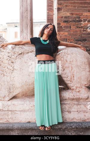 Selbstbewusste junge Frau, die in urbanem Ambiente ein Crop-Top und einen Maxirock mit Plisseedetail modelliert Stockfoto