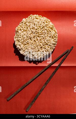Runder Block Instant Nudeln mit Holzstäbchen auf rotem Hintergrund, minimales Lebensmittelkonzept mit starkem Kontrast und Schatten Stockfoto