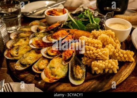 Eine üppige Platte mit Meeresfrüchten zeigt eine Auswahl an gebackenen Käsesmuscheln, pikanten Chilimuscheln und goldenen gebratenen Calamari, die auf einem rustikalen Wald präsentiert werden Stockfoto