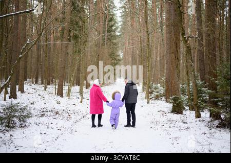 Familienspaziergang im Schnee. Mutter, Vater und Tochter machen einen Spaziergang durch verschneite Wälder, gehen auf verschneiten Pfaden und halten Hände. Eltern und Kinder verbringen ihre Weihnachtsferien im Freien Stockfoto