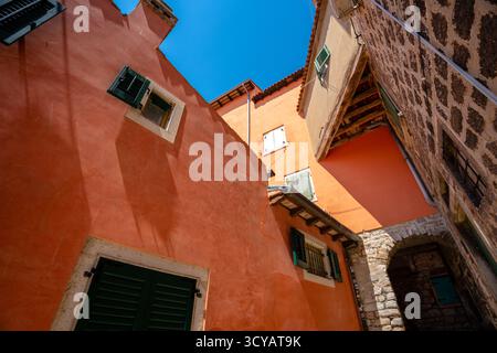 Rovinj, Kroatien - 14. August 2025: Eine sonnige Gasse mit Terrakotta- und Steinmauern, bunten Fensterläden und einem kleinen Bogen, der durch enge hinauf führt Stockfoto