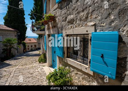 Rovinj, Kroatien - 14. August 2025: Charmante Kopfsteinpflasterstraße gesäumt von Steinhäusern mit hellen türkisfarbenen Fensterläden, eisengegrillten Fenstern und Stockfoto