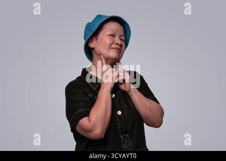 Lächelnde Frau in schwarzem Outfit mit blauem Eimerhut, die im Studio energetisch posiert Stockfoto