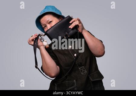 Frau mit hellblauem Jeansmütze hält schwarze Ledertasche und Schlüsselanhänger im Studio-Porträt Stockfoto