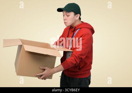 Junger Mann in rotem Hoodie mit offenem Karton, überraschtem Ausdruck, Innenaufnahmen im Studio Stockfoto