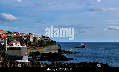Malerische Stadt an den Klippen mit roten Häusern, weißen Wänden und einem kleinen Leuchtturm mit Blick auf das ruhige Meer. Ein rot-weißes Schiff in der Nähe des Piers Stockfoto