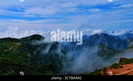 Neblige Berglandschaft mit dramatischen Klippen, Morgenlicht und rötlichen Felsen. Ätherische Wolken treiben durch grüne Täler. Perfekt für die Natur, Trav Stockfoto